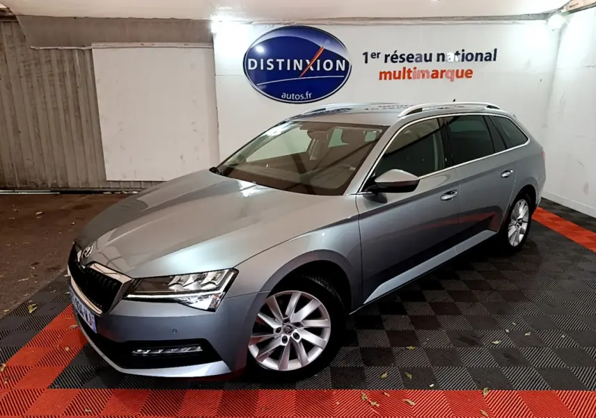 Vue 3/4 avant droite d'une Skoda Superb gris clair en break, stationnée en intérieur sur sol noir et rouge.
