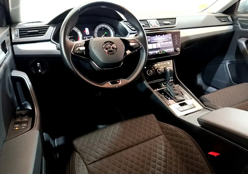 Intérieur de la Skoda Superb 2020 vu côté conducteur, volant cuir, console centrale avec écran tactile et sièges noirs matelassés.