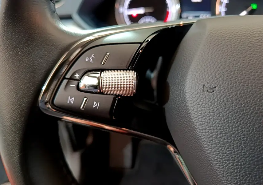 Gros plan sur la commande gauche du volant cuir d'une Skoda Superb gris clair, avec molette crantée et boutons multifonctions.