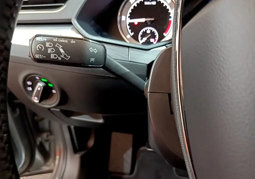 Gros plan sur la commande de régulateur de vitesse à gauche du volant cuir dans l'habitacle de la Skoda Superb gris clair 2020.