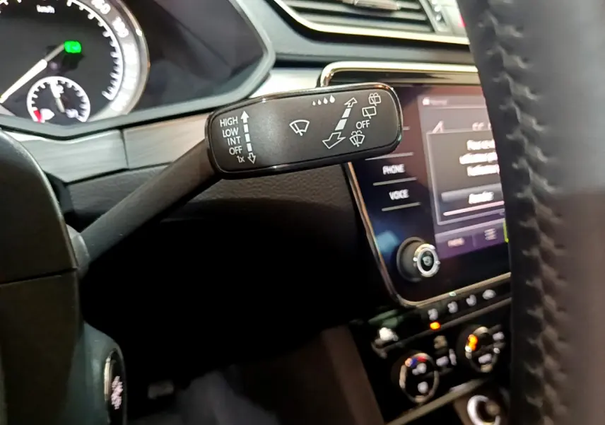 Gros plan sur la commande d’essuie-glace à gauche du volant cuir dans l’habitacle sombre d’une Skoda Superb gris clair.