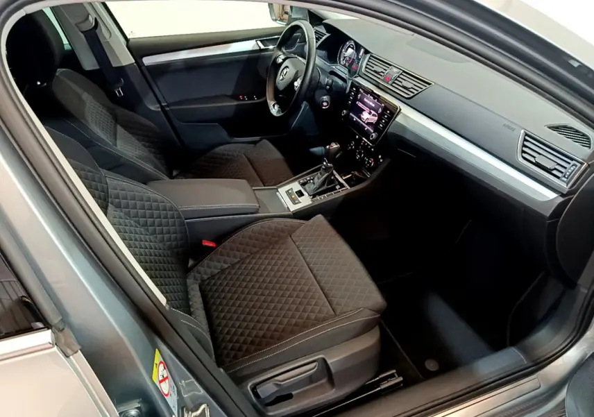 Intérieur de la Skoda Superb gris clair 2020 vu côté conducteur, sièges noirs matelassés et tableau de bord moderne avec écran tactile.