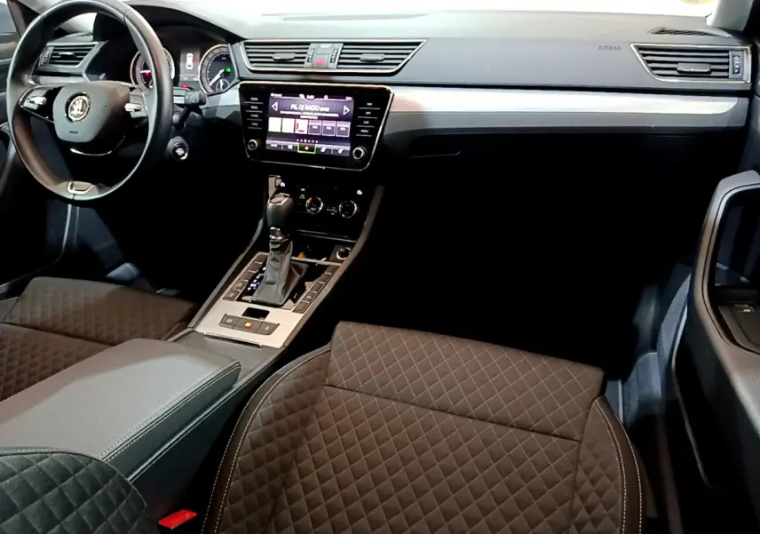 Intérieur de la Skoda Superb 2020 vu côté conducteur, sièges noirs matelassés et écran tactile central allumé.