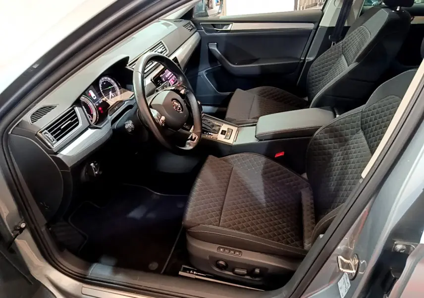 Intérieur côté conducteur de la Skoda Superb gris clair 2020, sièges noirs matelassés et tableau de bord moderne.