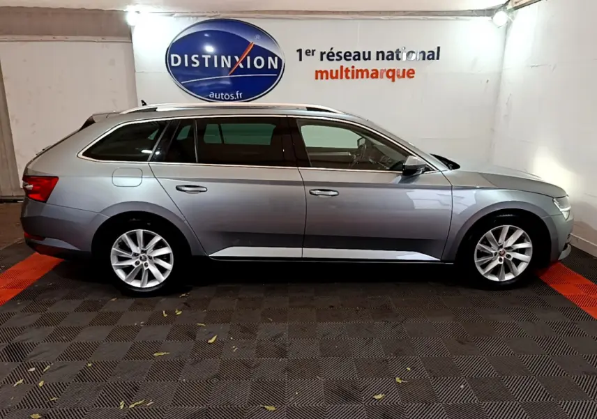 Profil côté droit d'une Skoda Superb gris clair 2020 en version break, stationnée en intérieur sur sol damier.