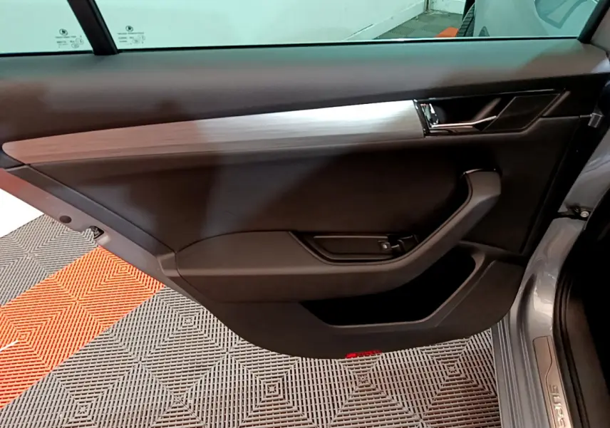 Vue intérieure de la porte côté gauche d'une Skoda Superb gris clair, avec garniture noire et insert décoratif argenté.