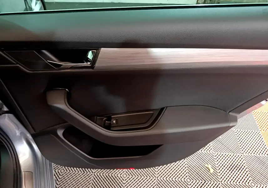 Intérieur côté gauche de la porte d'une Skoda Superb gris clair, avec poignée noire et insert décoratif bois clair.