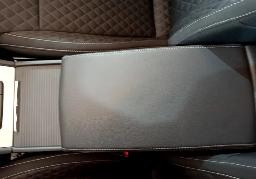 Gros plan sur l'accoudoir central en cuir noir avec surpiqûres blanches, entre les sièges marron matelassés de la Skoda Superb.