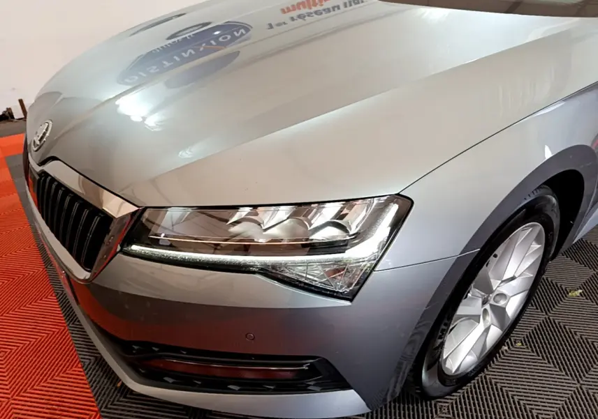 Vue 3/4 avant droit d'une Skoda Superb gris clair mettant en valeur ses phares LED et sa calandre chromée.