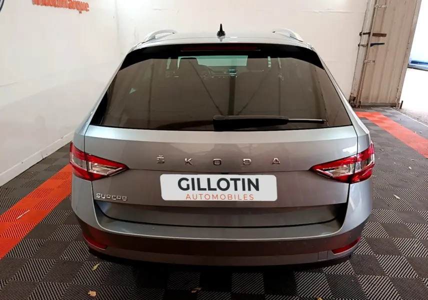 Vue arrière d'une Skoda Superb gris clair stationnée en intérieur avec feux arrière LED et logo visible.