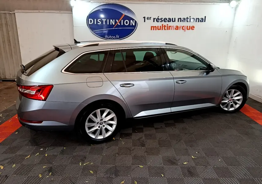 SKODA SUPERB break gris clair vu de profil côté gauche dans un showroom avec logo Distinxion en arrière-plan.