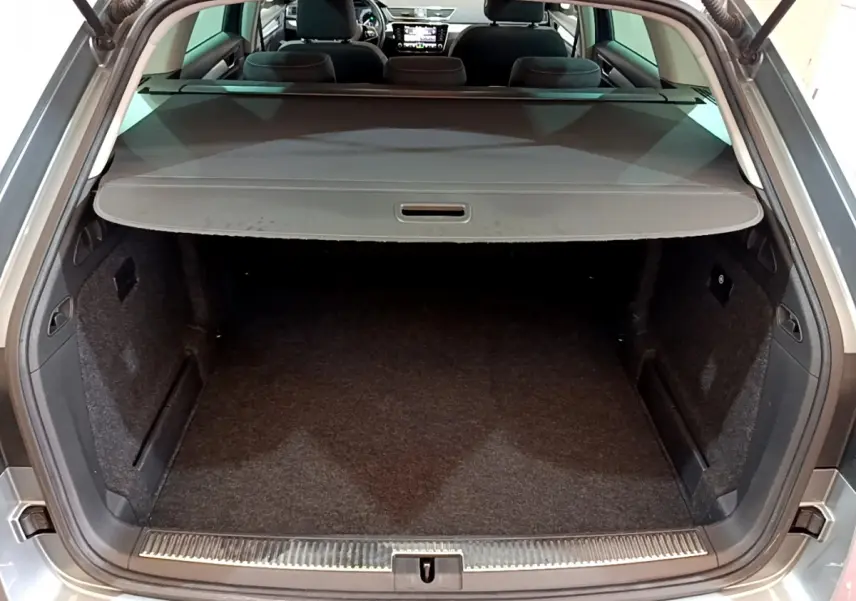 Coffre ouvert d’une SKODA SUPERB gris clair, vue arrière montrant l’espace de chargement et la tablette cache-bagages.