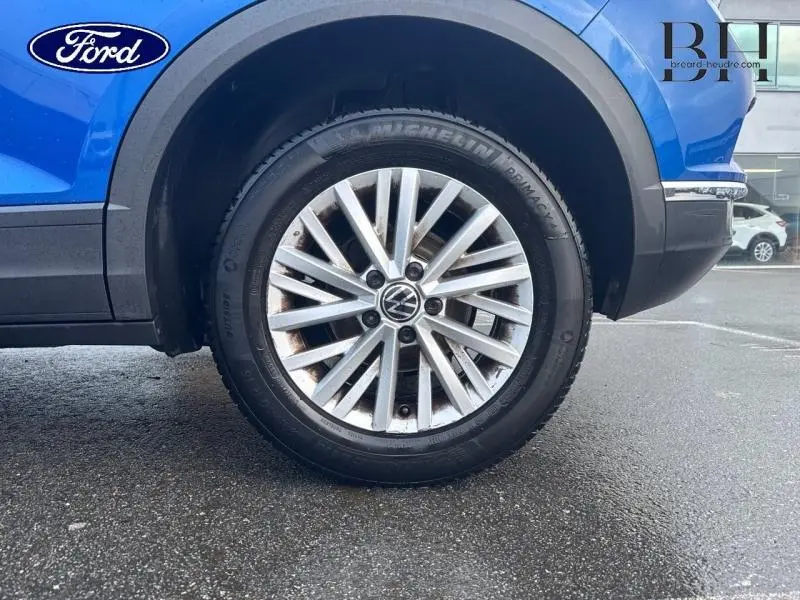 Gros plan sur la roue avant droite d’un Volkswagen T-Roc bleu Ravenna métallisé avec jante alu multibranches.