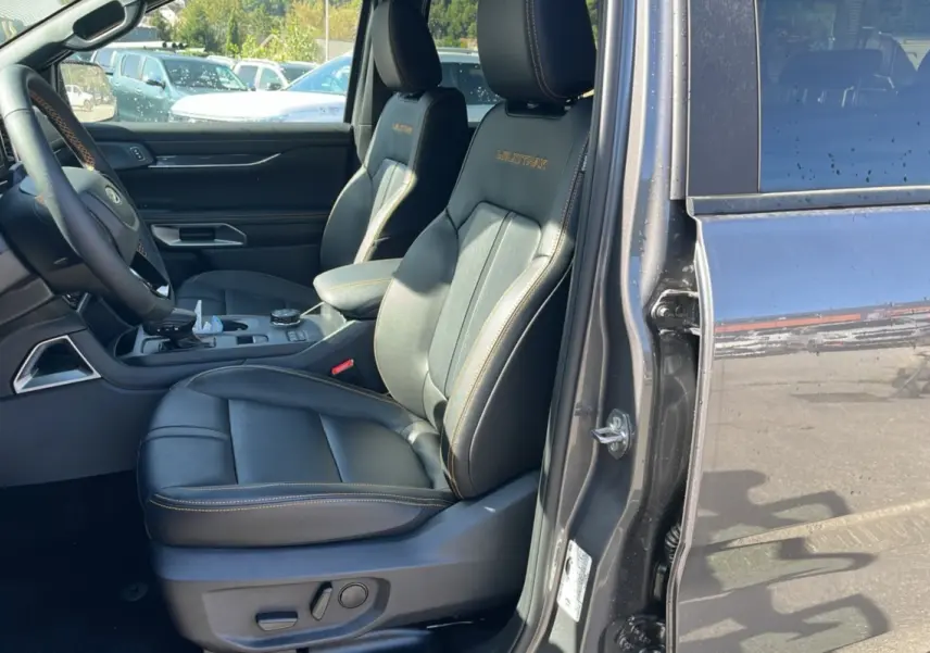 Vue intérieure côté conducteur du Ford Ranger PHEV gris carbone, mettant en valeur les sièges cuir Wildtrak avec surpiqûres orange.