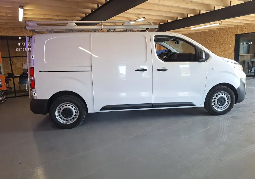 Vue de profil côté droit d'un utilitaire blanc Citroën Jumpy 2.0 BlueHDi 120 Club avec galerie de toit en intérieur.