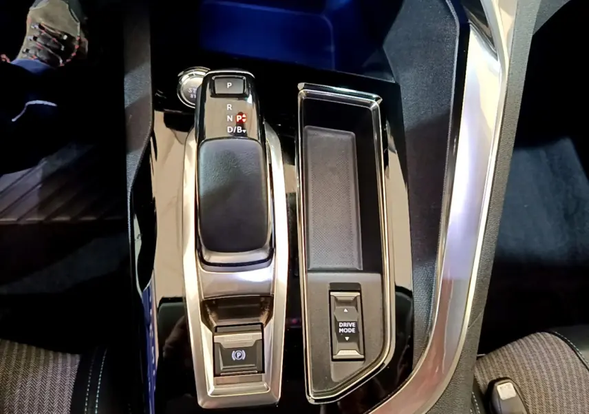 Vue rapprochée de la console centrale noire brillante du Peugeot 3008 hybride avec levier de vitesses et bouton Drive Mode.