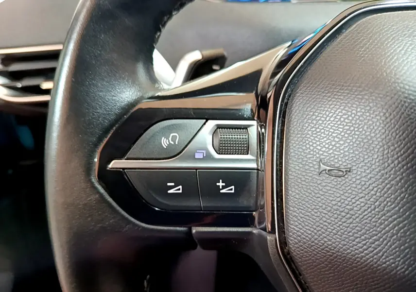 Gros plan sur les commandes gauche du volant cuir noir du Peugeot 3008 hybride bleu, avec boutons multifonctions.