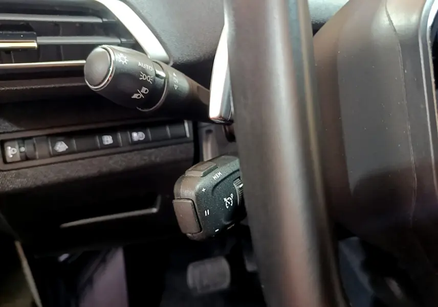 Gros plan sur les commandes au volant et la manette d'éclairage du Peugeot 3008 hybride bleu, intérieur noir.