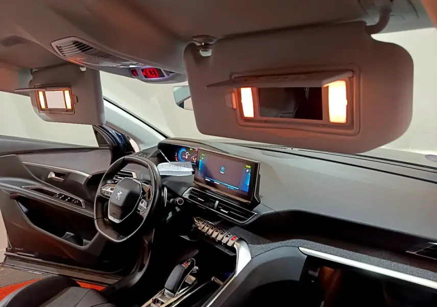 Intérieur du Peugeot 3008 bleu 2021, vue côté conducteur, tableau de bord numérique et miroirs de courtoisie éclairés.