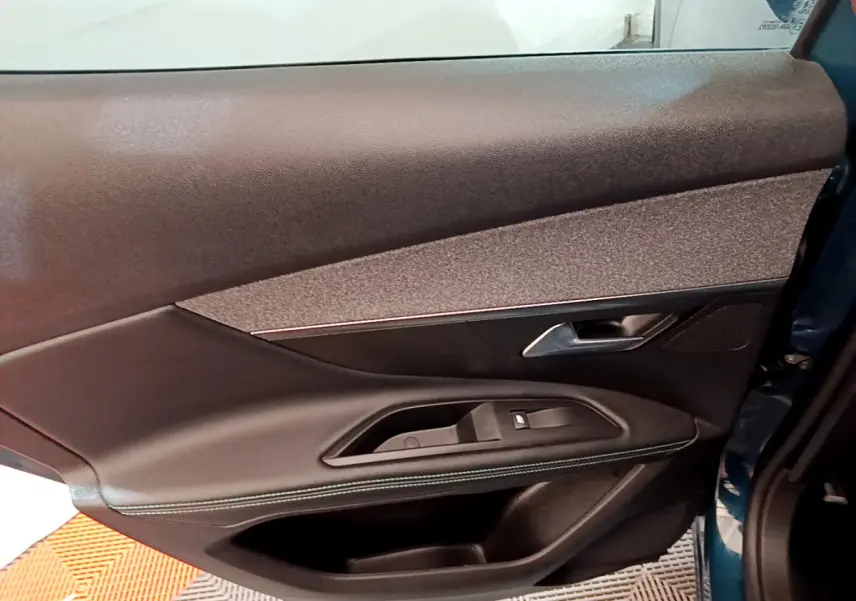 Gros plan sur la porte côté gauche intérieure du Peugeot 3008 bleu, avec garniture noire et bouton de vitre électrique.
