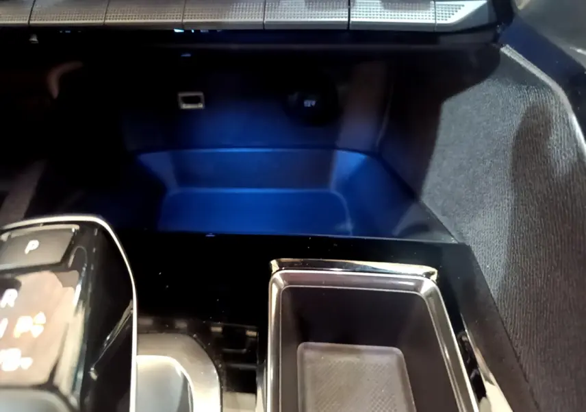 Gros plan sur la console centrale noire brillante du Peugeot 3008 bleu, avec levier de vitesses automatique et prise 12V visible.