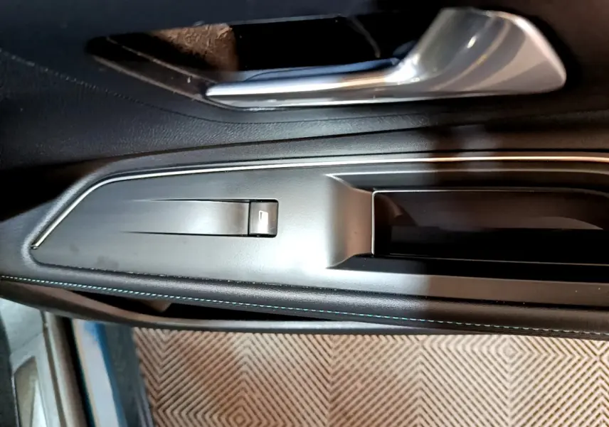 Gros plan sur la poignée intérieure côté gauche de la porte d’un Peugeot 3008 bleu avec bouton de lève-vitre intégré.