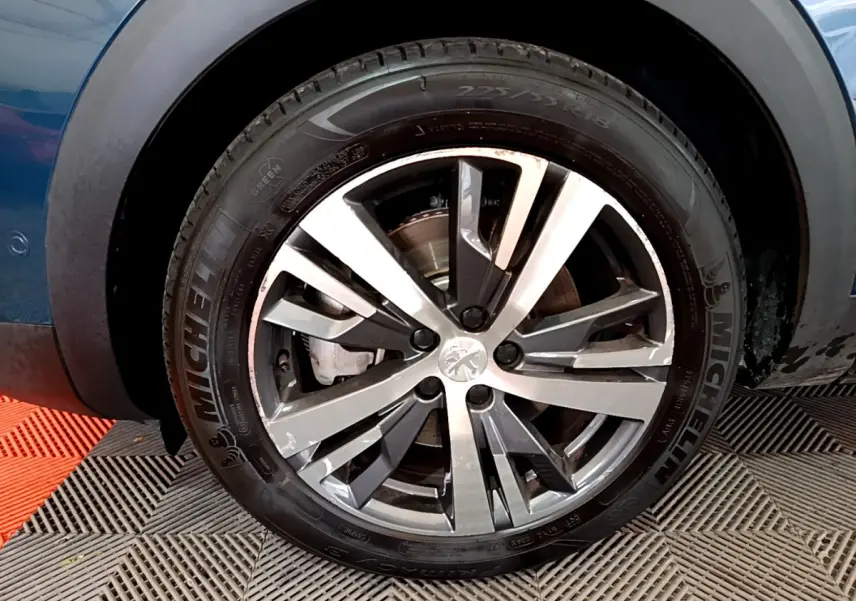 Gros plan sur la roue avant gauche du Peugeot 3008 bleu, mettant en valeur la jante alliage et le pneu Michelin.