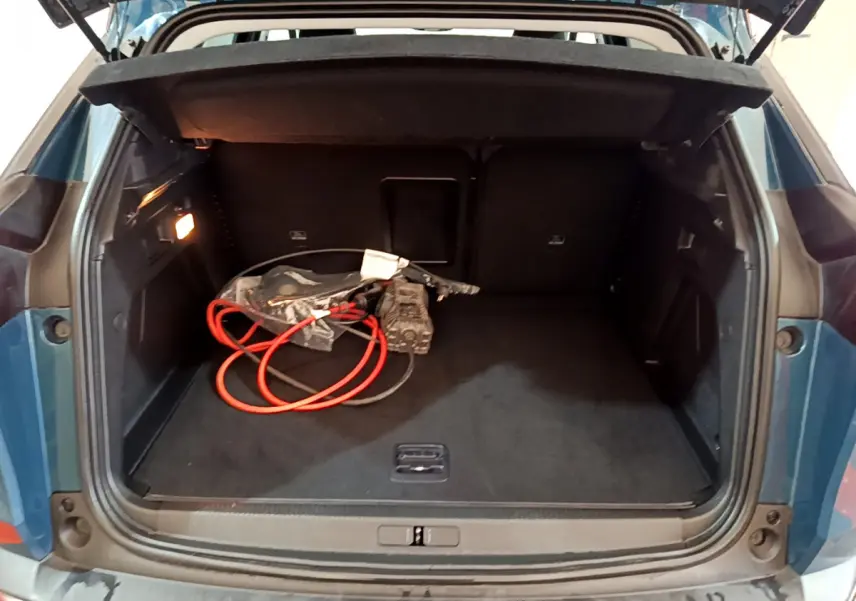 Coffre ouvert d’un Peugeot 3008 bleu, vue arrière montrant un câble de recharge hybride et un intérieur spacieux noir.