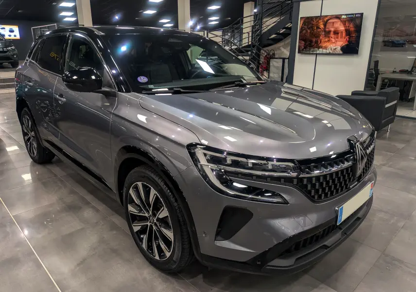 Renault Austral gris schiste avec toit noir, vue 3/4 avant en intérieur, mettant en valeur sa calandre et ses jantes biton.