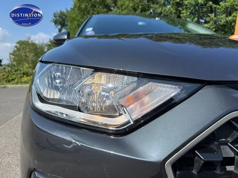 Gros plan sur le phare avant droit d'une Audi A1 Sportback noir Mythic métallisé sous un ciel bleu.