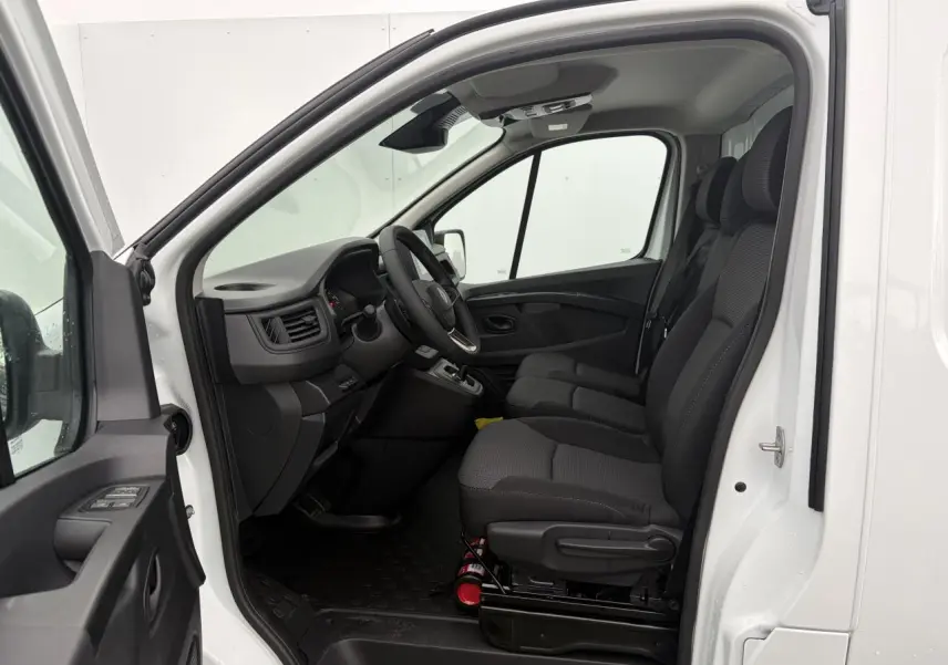 Vue intérieure côté conducteur du Renault Trafic Fourgon blanc glacier, montrant les sièges avant en tissu et le tableau de bord.