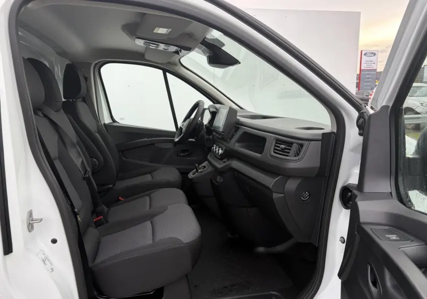 Vue intérieure côté conducteur du Renault Trafic Fourgon blanc Glacier, montrant les sièges tissu et le tableau de bord avec écran tactile.