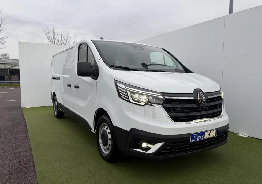 Renault Trafic Fourgon blanc glacier vu en 3/4 avant droit, avec projecteurs LED allumés et jantes tôles 16 pouces.