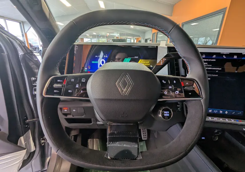 Vue rapprochée du volant noir avec surpiqûres tricolores du Renault Austral E-Tech 200, tableau de bord numérique en arrière-plan.