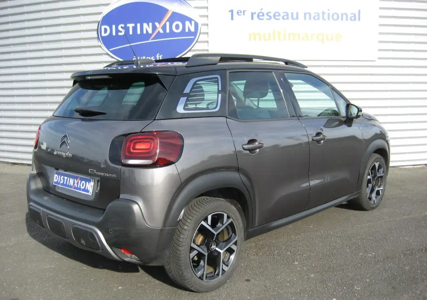 Vue 3/4 arrière droite d'un Citroën C3 Aircross gris platinium avec jantes noires et toit noir.