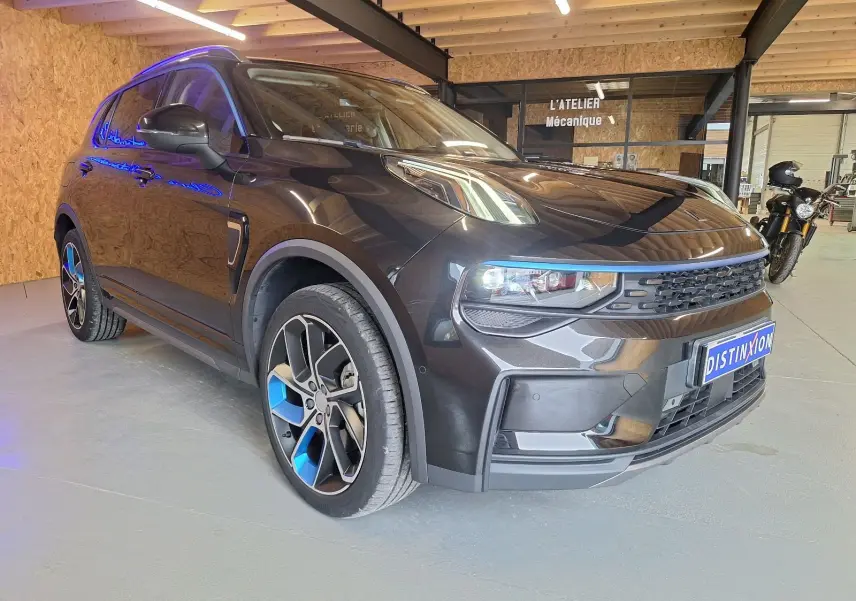 Lynk & Co 01 noir en 3/4 avant droit, avec jantes bicolores bleu et noir, dans un atelier mécanique intérieur.