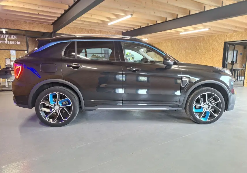 Vue latérale droite d'un LYNK & CO 01 noir 2023 avec jantes bicolores et feux arrière allumés en intérieur.