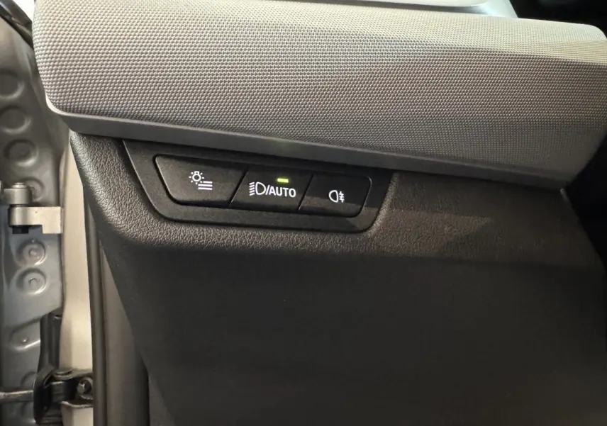 Gros plan sur les commandes d’éclairage automatiques et antibrouillard à gauche du tableau de bord d’une BMW X1 gris foncé 2024.