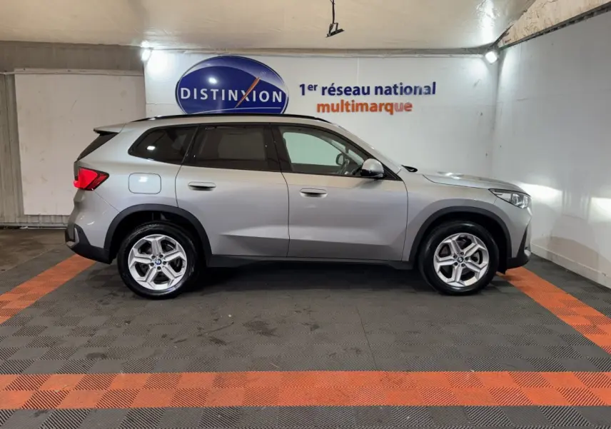 Vue de profil côté gauche d’un BMW X1 sDrive20i Business Design gris foncé dans un showroom intérieur.