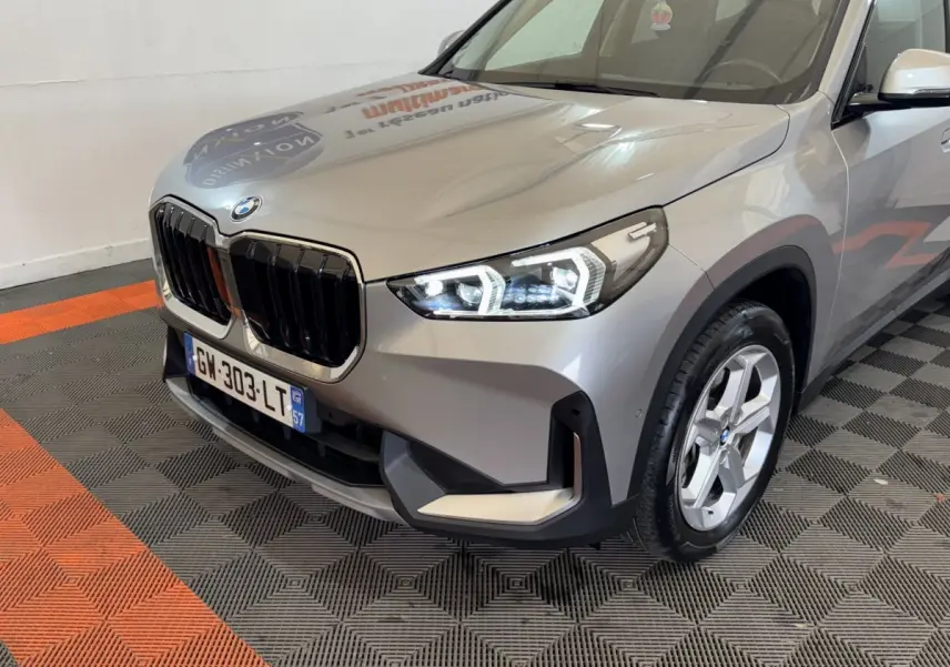 BMW X1 sDrive20i gris foncé vue 3/4 avant droit, avec calandre noire et phares LED allumés.