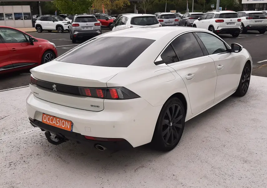 Vue 3/4 arrière droite d'une Peugeot 508 blanche de 2019 avec jantes noires et vitres teintées, en stationnement extérieur.