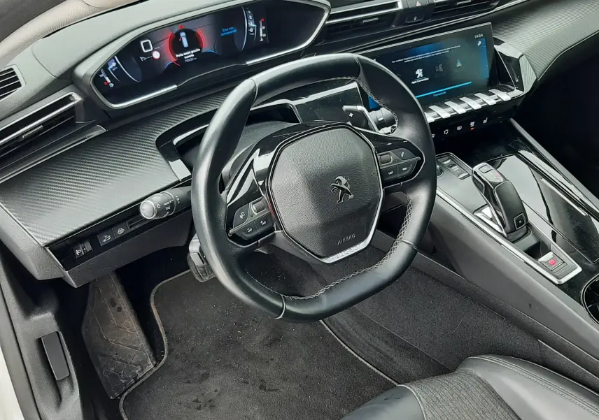 Vue intérieure côté conducteur de la Peugeot 508 blanche, avec volant compact et tableau de bord numérique moderne.