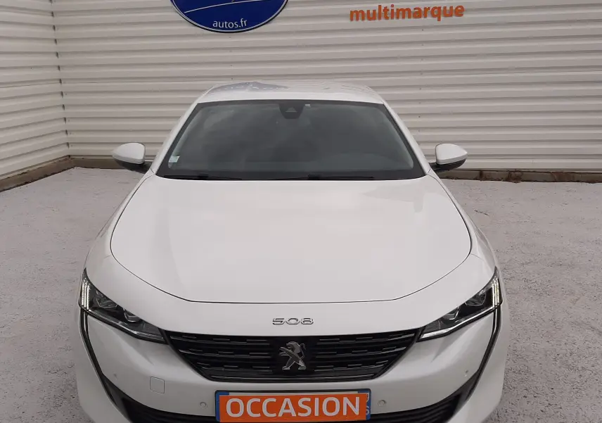 Vue avant frontale d'une Peugeot 508 blanche avec calandre noire et plaque orange "OCCASION" en concession.