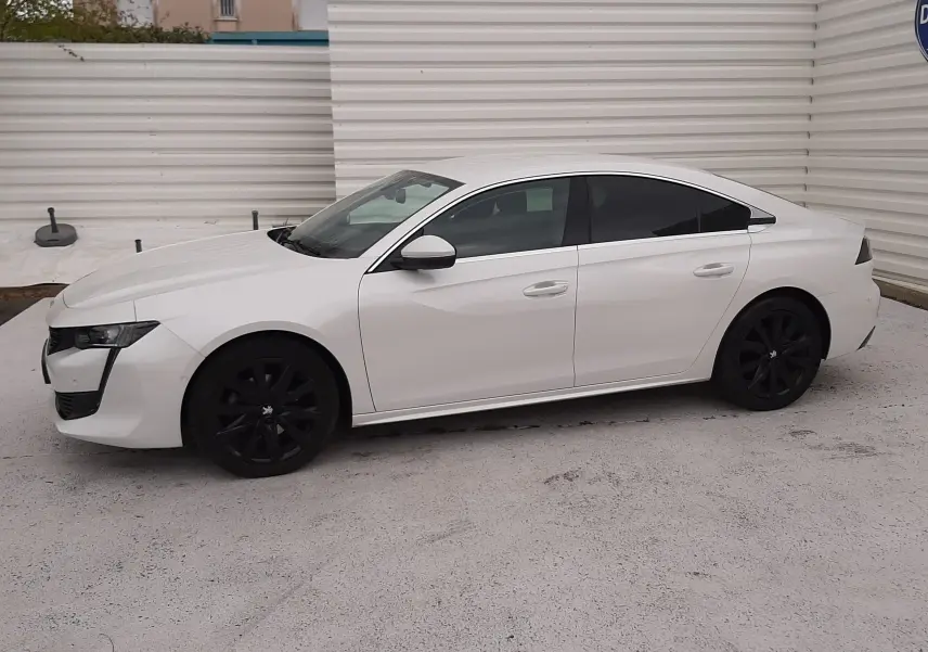 Peugeot 508 blanc vue de profil côté gauche, avec jantes noires et vitres teintées, stationnée sur sol clair.