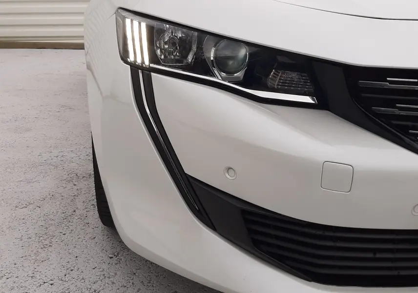 Gros plan sur l'avant gauche blanc d'une Peugeot 508 2019, mettant en valeur son phare LED vertical et la calandre noire.
