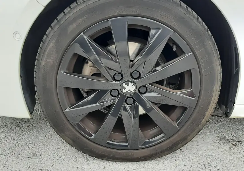 Gros plan sur la roue avant droite d'une Peugeot 508 blanche avec jante alliage noire au design moderne.