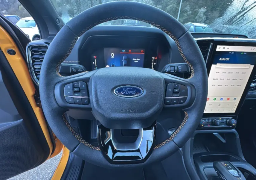 Vue intérieure centrée sur le volant cuir avec surpiqûres orange du Ford Ranger Cyber orange, tableau de bord et écran tactile visibles.
