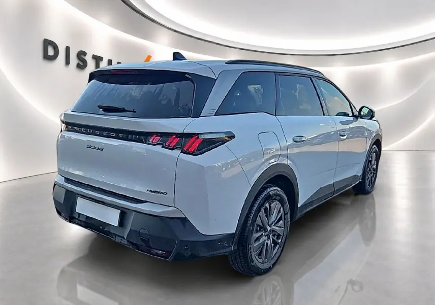Vue 3/4 arrière droit d'un Peugeot 5008 Hybrid blanc avec feux arrière LED et vitres arrière surteintées dans un showroom.