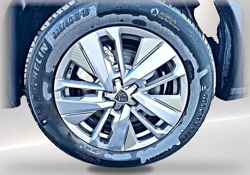 Gros plan sur la jante alu 18 pouces Michelin d’un Peugeot 5008 blanc, mettant en valeur le logo Peugeot central.