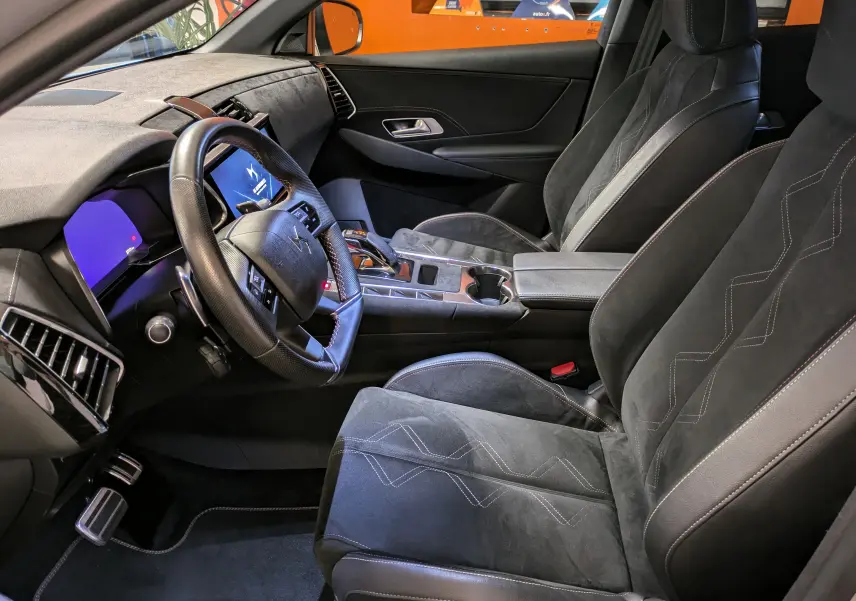 Vue intérieure côté conducteur du DS7 2023 avec sièges Alcantara noirs et tableau de bord moderne au volant cuir.